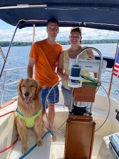 Couple and their dog taking the helm on on 2nd Wind sailboat on grand traverse bay in Traverse City, Michigan with WIND Sailing.