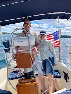 Couple taking the helm on 2nd Wind sailboat on grand traverse bay in Traverse City, Michigan with WIND Sailing.